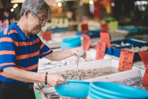 an active senior asian chinese grandfather buying squid from the fish stall in wet market