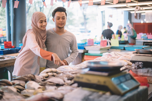 an asian malay couple shopping at fish stalll choosing fish for their dinner cooking later during weekend