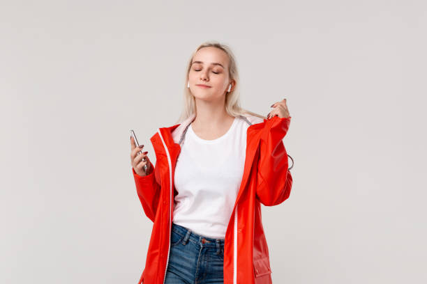 menina consideravelmente loura que desgasta o raincoat vermelho e a dança branca do t-shirt que escuta a música com earbuds sem fio. conceito de apreciar a vida. - top hat audio - fotografias e filmes do acervo