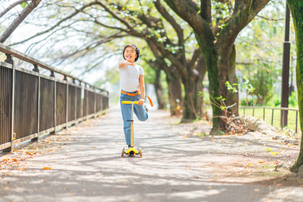 A little girl is riding a push scooter happily in a public park in summer.