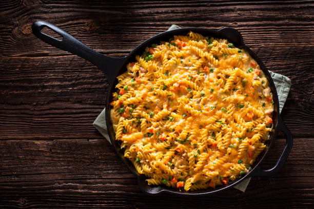 Cheesy Pasta Skillet Pasta Chicken Casserole in a Cast Iron Skillet with Cheddar Cheese, Peas, Carrots and Cream fusilli stock pictures, royalty-free photos & images