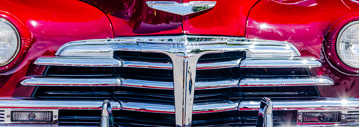 Panoramic close-up view of a  vintage car's grill and red bodywork with sunspot reflections..