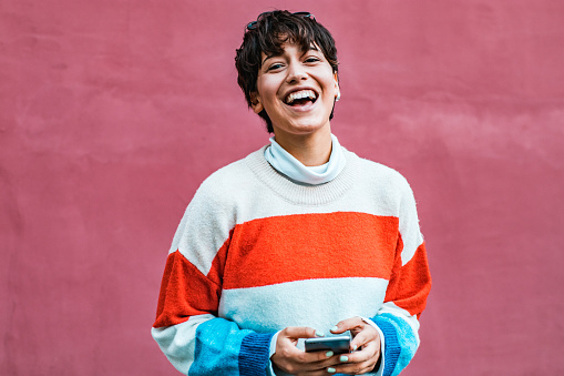 a young girl with short hair standing by the wall while holding a cellphone in her hand and smiling