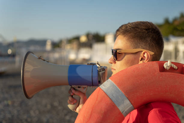 joven socorrista con megáfono en el fondo de la playa. socorrista de guardia con una boya salvavidas en la playa - marine safety equipment audio fotografías e imágenes de stock