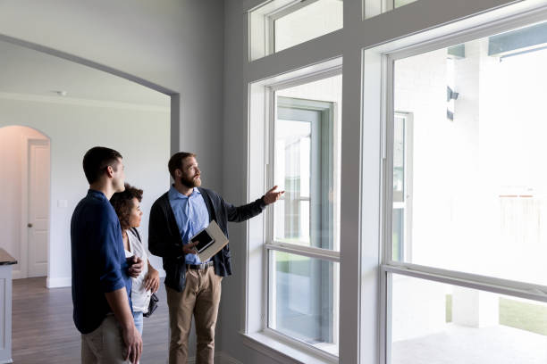 Male Real Estate Agent shows a couple a beautiful home Confident male real estate agent gestures toward a beautiful view out the window of a new home. Interested potential homeowners attentively listen to the real estate agent. real estate agent male stock pictures, royalty-free photos & images