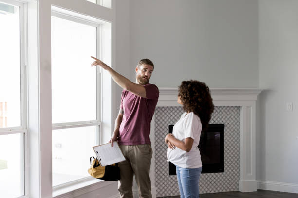 Home inspector points to something outside while talking with homeowner Serious home inspector or handyman points to something outside of a window while talking with pregnant homeowner. inspector stock pictures, royalty-free photos & images