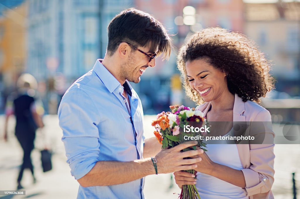 Man is giving flowers to his date on the street Couple - Relationship Stock Photo