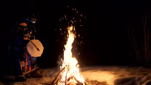 The shaman performs a dance with a tambourine around the fire.