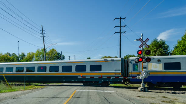 Passenger train cars moving past a level crossing gate on a road in the summer Passenger train cars moving past a level crossing gate on a road in the summer railway signal stock pictures, royalty-free photos & images