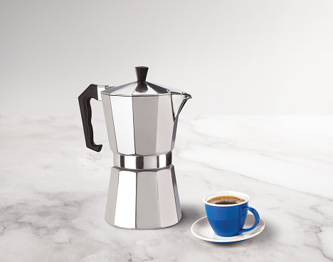 stovetop espresso maker with a coffee cup on a marble countertop