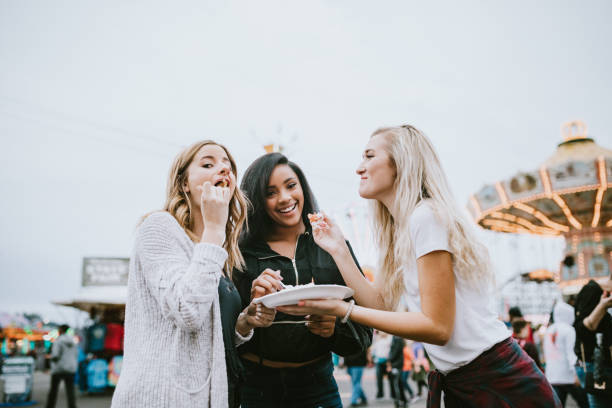 Teenage Women Friend Group Enjoying State Fair A group of girl friends spend time together at their local county fair carnival, tasting fun foods and trying out an assortment of amusement park rides. agricultural fair stock pictures, royalty-free photos & images