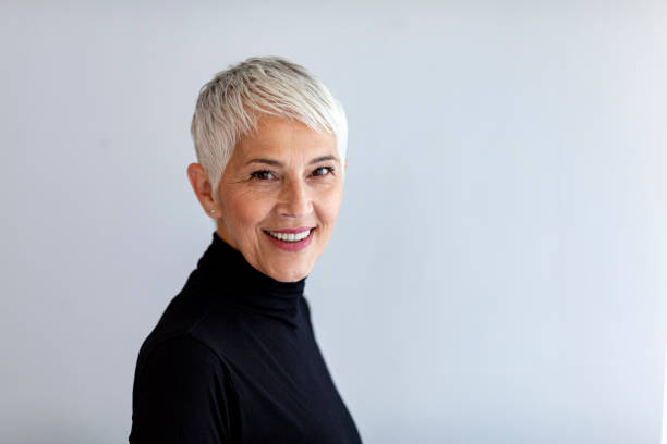 Happy smiling mature woman Elegant mid adult short gray hair woman against gray background. Stylish mature woman in black turtleneck, looking at the camera and smiling. white hair stock pictures, royalty-free photos & images