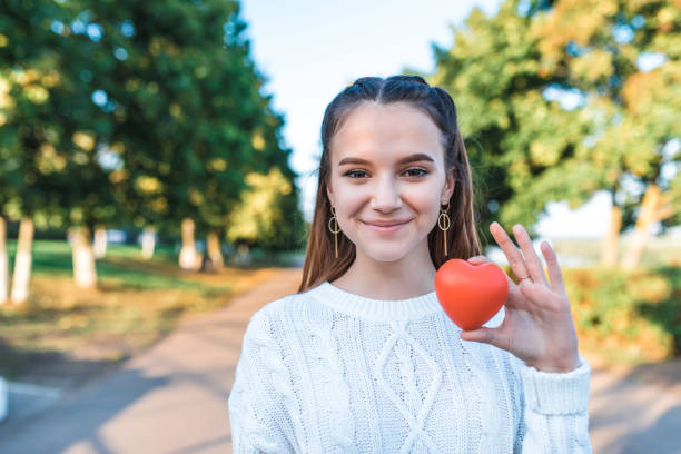 Happy cheerful teenage girl 13-15 years old, summer autumn spring in park, red heart in her hand. Free space text. Concept give love, donation wish of love, help children, save life, positive joy. stock photo