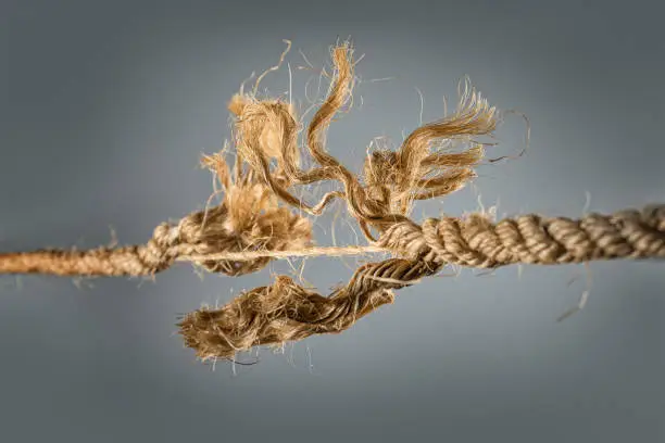 Frayed rope near to break on gray background. Selective focus