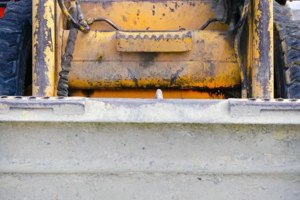 front side of an old little scratched orange bulldozer. building background. tractor bucket smeared in sand