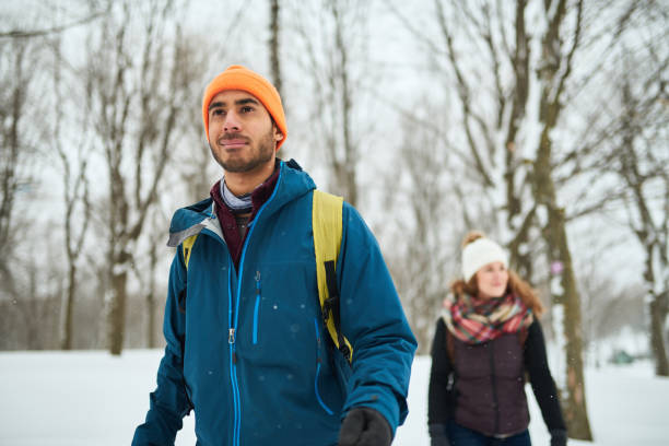 Happy multi-ethnic friends of caucasian and indian ethnicity hiking in a snow covered national park during holiday season