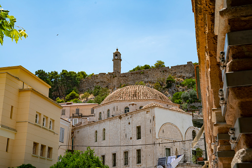 Domed roof of town hall below historic stone wall and clock tower on hill from the street of Nafplio, Greece.