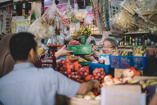 an asian chinese senior man as owner of the spice store receiving basket of products from his customer for price calculation at the spice stall