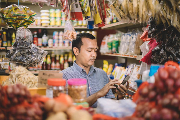 un malay asiatique mi adulte calculant le coût des articles sélectionnés de son client - grocer photos et images de collection