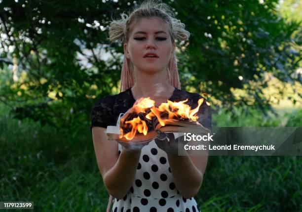 Girl Holds A Burning Book In Her Hands A Young Woman In A Forest Burns A Book Stock Photo - Download Image Now