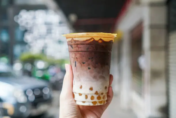A Plastic cup of dark chocolate with milk and golden bubble/boba pearls.