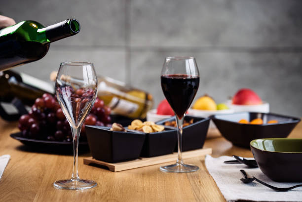 Red wine pouring into a wine glass at a tasting with various types of appetizers. stock photo