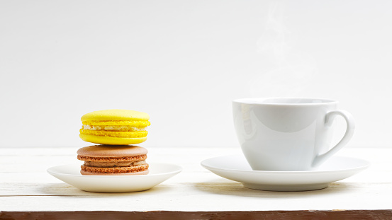 A cup of coffee and two macaroons lemon and chocolate on white wooden table. Front view
