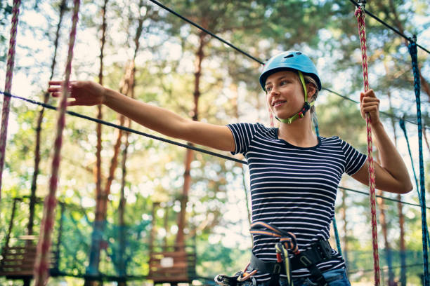Teenage girl enjoying ropes course Teenage girl in ropes course in adventure park. The girl is reaching for the line.
Sunny summer day.
Nikon D850 canopy tour photos stock pictures, royalty-free photos & images