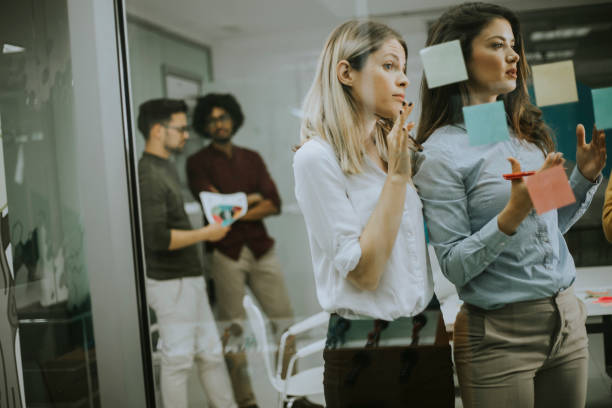 istock Young business women discussing in front of glass wall using post it notes and stickers 1179137541