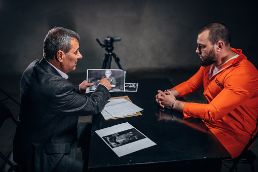 Prisoner in orange jumpsuit with handcuffs and detective sitting in the investigation room