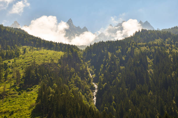 Scenic view of the Mont Blanc massif with the Aiguilles de Chamonix shrouded by mist in the background and a waterfall on a slope covered by forests in summer, Chamonix-Mont-Blanc, Haute Savoie, France
