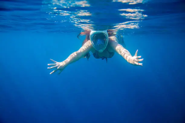 Snorkeling girl in full-face snorkeling mask undersea. Woman swimming. Warm shallow sea water coral reef. Underwater photo of oceanic landscape. Active seaside vacation. Water sport in tropical sea