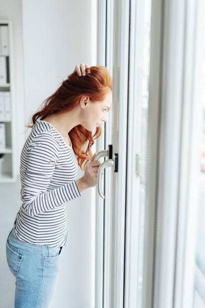istock Young woman standing watching through a glass door 1179146759