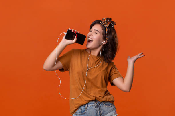 hübsche brünette frau in einem t-shirt und schöne stirnband tanzen hören musik mit kabelgebundenen kopfhörer über orange hintergrund isoliert. das leben genießen - adolescence beautiful lifestyles studio stock-fotos und bilder