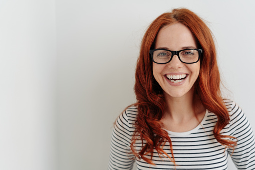 Portrait of a beautiful cheerful young woman with long curly red hear laughing happy while wearing eyeglasses with black frames and a striped long sleeve T-shirt