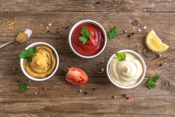 Three classic sauces  ketchup, mayonnaise and mustard on wooden background. Set of popular american sauces, top view, copy space.