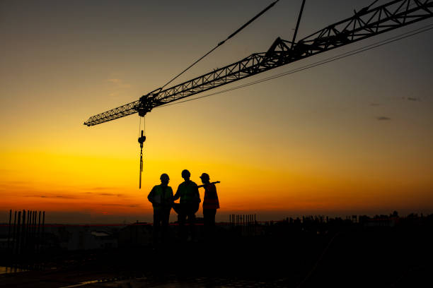 Developing the city for the better together Photo of three Businessman Silhouette engineer standing under the tower crane working late, looking a building site and career growth concepts. Construction site with sunset. serbia photos stock pictures, royalty-free photos & images