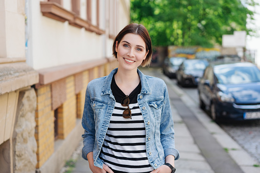 Smart trendy young woman standing in the street with her hands in her pockets smiling at the camera