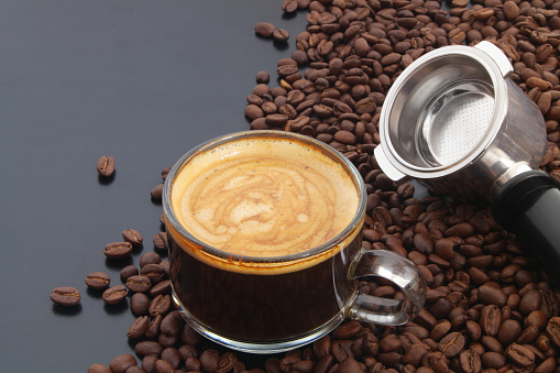 Cup of coffee and roasted coffee beans with coffee maker filter on black table