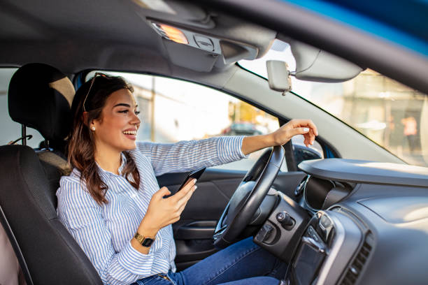 Business woman sitting in car and using her smartphone. Portrait of a young woman texting on her smartphone while driving a car. Business woman sitting in car and using her smartphone. Mock up image with female driver and phone screen drivers seat stock pictures, royalty-free photos & images