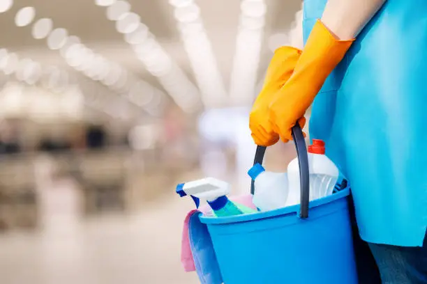 The cleaning lady standing with a bucket and cleaning products on blurred background.