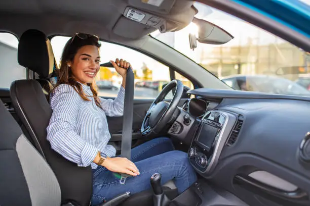 Safety first. Beautiful Caucasian lady fastening car seat belt. Pretty young woman driving her new car. Pretty young woman driving her new car. Female fastening safety belt in car