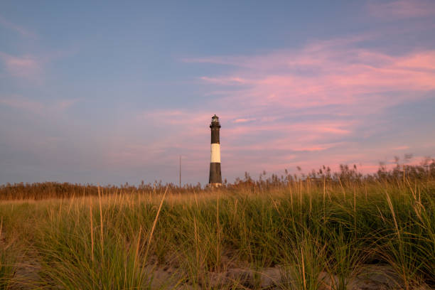 istock Soft pink pastel colors in the sky behind a lighthouse with warm light still on the beachgrass. Fire Island Lighthouse, New York 1179164151
