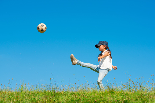 Girl kicking soccer ball on meadow