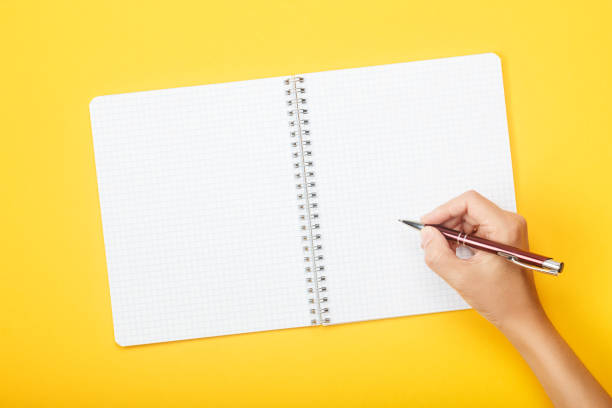 istock Hand with pen over blank notebook on a yellow background. Mock up with copy space for your ideas. 1179169532