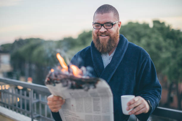 verticale d'homme barbu de sourire affichant le journal (sur le feu) - magazine brûlant dans les mains de l'homme - concept chaud et de nouvelles de rupture - reading newspaper men magazine photos et images de collection