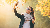 Portrait of pretty smiling brunette woman taking selfie on smartphone In autumn sunny garden
