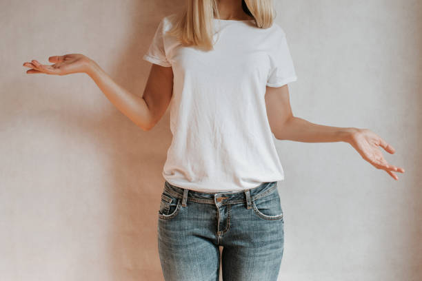 Blond hair woman posing near a light wall. Beautiful young caucasian girl. Hand gestures. Emotion. Casual clothing. Studio model in work. Strong woman, future is female. Jeans and white blank t-shirt stock photo