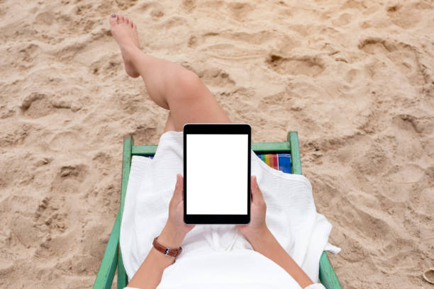 istock a woman holding and using a black tablet pc with blank desktop screen while lying down on a beach chair 1179176718