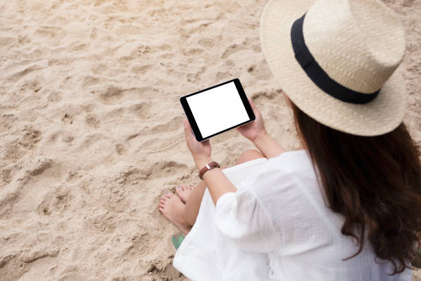 istock a woman holding a black tablet pc with blank desktop screen while sitting on a beach chair 1179176720